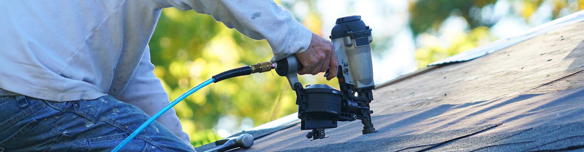 Handyman Using Nail Gun To Install Shingle To Repair Roof